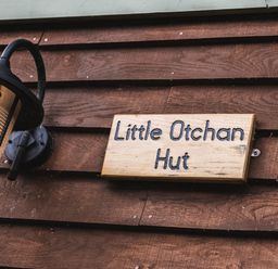 A wooden sign that says Little Otchan Hut next to a wall-mounted lantern on a wooden wall at Little Otchan Shepherd's Hut in Halsham near Roos