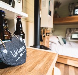 A wooden countertop with two bottles and a heart shaped welcome sign in a small cabin bedroom at Little Otchan Shepherd's Hut Halsham near Roos