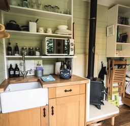 A small kitchen area with a sink microwave open shelves and a stove next to a bed at Little Otchan Shepherd's Hut in Halsham near Roos