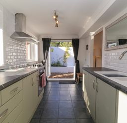 A kitchen with a stove oven and sink with a faucet and open doors to a garden at The Corner House in Ufford near Woodbridge