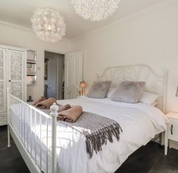 A bedroom with a white metal bed frame two fluffy pillows and a blanket on the bed a white nightstand with a lamp and a wardrobe with patterned doors at The Corner House in Ufford near Woodbridge