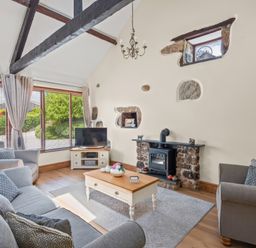 A living room with sofas coffee table wood burning stove and large window at The Dairy in St Neot