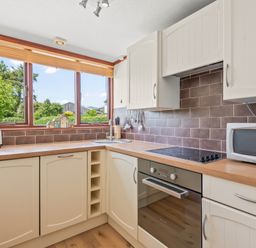 A kitchen with white cabinets wooden countertops a microwave toaster and an electric stove at The Dairy in St Neot