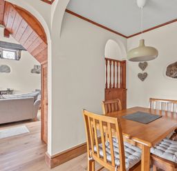 A dining area with a wooden table and four chairs next to an archway leading to a living room at The Dairy in St Neot