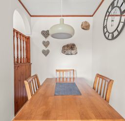 A dining room with a wooden table and chairs a hanging light a wall clock and heart decorations at The Dairy in St Neot