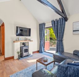 A living room with a leather sofa television and wood-burning stove at The Stables in St Neot