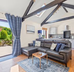 An open living room and kitchen with a leather sofa and small table near an open door to a patio at The Stables in St Neot