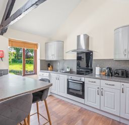 A kitchen with grey cabinets and appliances and a breakfast bar with stools at The Stables in St Neot