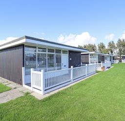 A group of modern single storey holiday chalets with white fences and green lawns at 104 The Laurels in Chapel St Leonards