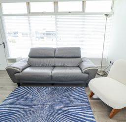 A living room with a grey sofa a white chair a blue striped rug and a standing lamp at 104 The Laurels in Chapel St Leonards