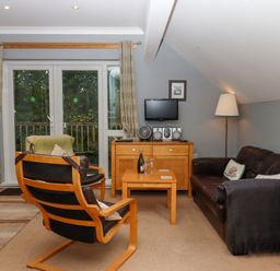A sitting room with leather armchairs a wooden table a floor lamp and a TV on a wooden cabinet at 5 Lakeview Rise Highampton near Hatherleigh
