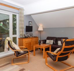 A living room with two wooden framed chairs a leather sofa wooden tables a sideboard and glass doors at 5 Lakeview Rise Highampton near Hatherleigh