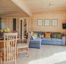 A living room with a dining table and chairs a blue sofa and a wall-mounted tv at Foxglove in Higher Wambrook near Chard