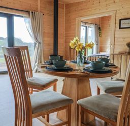 A dining area with wooden chairs and a round table set with dishes and a vase of yellow flowers at Foxglove in Higher Wambrook near Chard