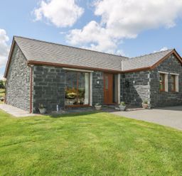 A stone house with wooden door and windows surrounded by lawn at Bwthyn Clyd in Llanddaniel Fab