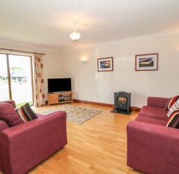 A living room with two red sofas and a television near a sliding glass door at Bwthyn Clyd in Llanddaniel Fab