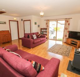 A living room with red sofas a wooden cabinet a television and a bookcase at Bwthyn Clyd in Llanddaniel Fab