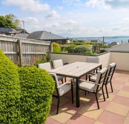 An outdoor patio with a dining table and six chairs overlooking rooftops and the sea at Karenza in Penzance