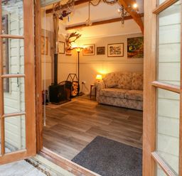 A sitting room with a floral sofa a wood burning stove and framed pictures on the wall at The Cabin at Little Timbers Ringwood