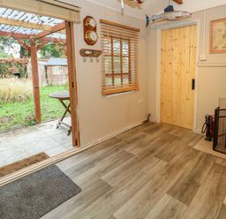 A room with wood flooring a small wood stove a wooden door and an open door leading to a garden at The Cabin at Little Timbers Ringwood