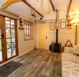 A living room with a sofa wood stove wooden door and glass doors leading outside at The Cabin at Little Timbers in Ringwood