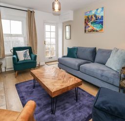 A living room with a blue sofa a green armchair a wooden coffee table and a painting on the wall at Honeypot Cottage in Swanage