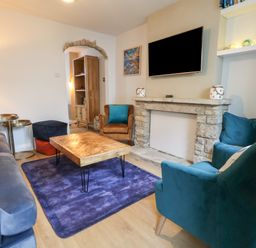 A living room with a blue sofa teal armchairs wooden coffee table stone fireplace and a wall-mounted TV at Honeypot Cottage in Swanage