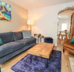 A living room with a blue sofa a wooden coffee table a brown armchair and a floor lamp at Honeypot Cottage in Swanage