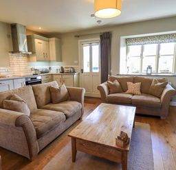 A living room with two sofas and a wooden coffee table next to a kitchen area at Fox Howe in Thornthwaite