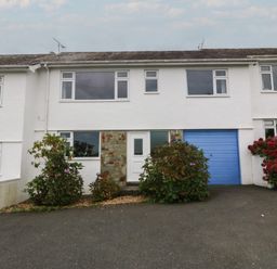 A white two-story house with a blue garage door and bushes in front at Ty Nant in Abersoch