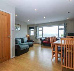 A living room with two sofas a dining table and chairs next to a large window at Ty Nant in Abersoch