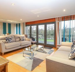 A living room with two beige sofas a glass coffee table and large windows overlooking a river at Tealby in Horning