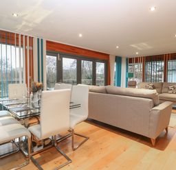 A living room and dining area with glass table white chairs and beige sofas at Tealby Horning
