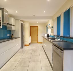 A modern kitchen with white cabinets blue backsplash and tiled floor at Tealby in Horning