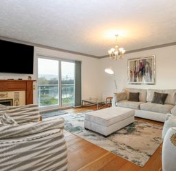 A living room with sofas a wooden floor a fireplace a large window and a chandelier at White Gables in Horning