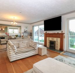 A living room with patterned sofa a fireplace and mounted tv overlooking a garden at White Gables in Horning