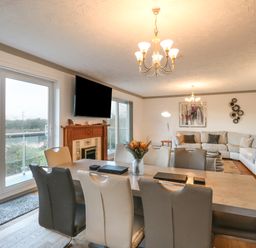 A dining area with a table and chairs next to a living room with sofas a fireplace and a wall-mounted TV at White Gables in Horning