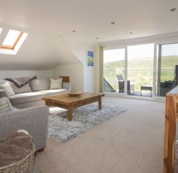 A living room with grey sofas wooden coffee table and sliding glass doors opening to a balcony at Atlantic View in Holywell Bay