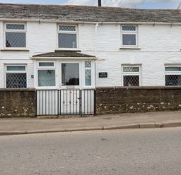 The exterior of a white brick cottage with multiple windows and a gated front entrance at Crab Cottage in Delabole