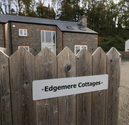 A wooden fence with a sign that says Edgemere Cottages and stone cottages in the background at Edgemere Cottage in Cartmel