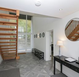 An entryway with wooden stairs glass doors a black console table with lamps and a round mirror at Edgemere Cottage in Cartmel