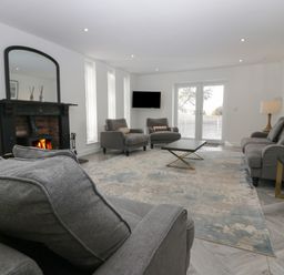 A living room with gray sofas a fireplace a coffee table and a wall-mounted tv at Edgemere Cottage in Cartmel
