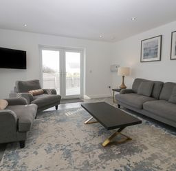 A living room with gray sofas a black coffee table a wall-mounted TV and two framed pictures at Edgemere Cottage in Cartmel