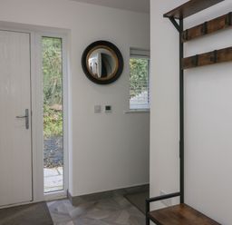 An entrance area with a white door a narrow window a round mirror on the wall and a wooden bench with coat hooks at Edgemere Retreat in Cartmel