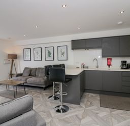 A kitchen and living area with a gray sofa wooden coffee table bar stools and framed plant pictures at Edgemere Retreat in Cartmel