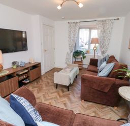 A living room with brown sofas a wall-mounted TV and a wooden sideboard at Coastal Retreat in Seahouses
