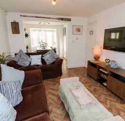 A living room with brown sofas cushions a green ottoman a wooden TV stand and a wall-mounted TV at Coastal Retreat in Seahouses
