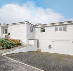 A white single-story house with a driveway shrubs and a garage at Seamay in Polzeath