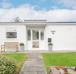 Front entrance of white single story house with glass door bench and garden at Seamay Polzeath