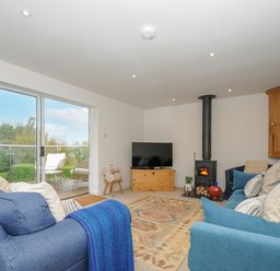 A living room with blue sofas a wood stove a television and glass doors leading to a balcony at Seamay in Polzeath